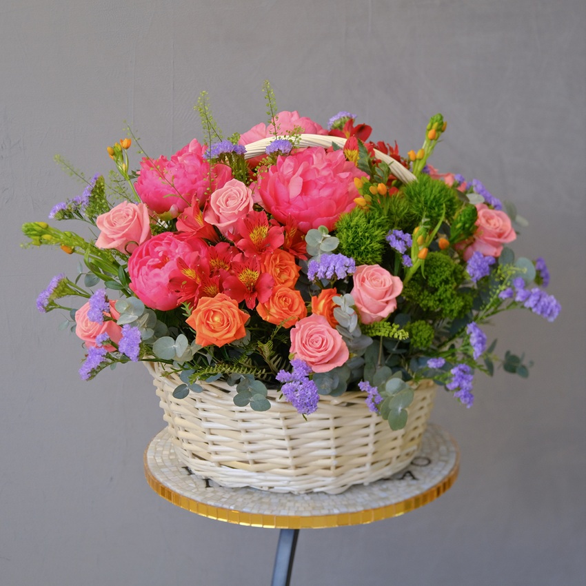 Коралловые пионы и кустовые розы в яркой корзине "Закат над океаном"