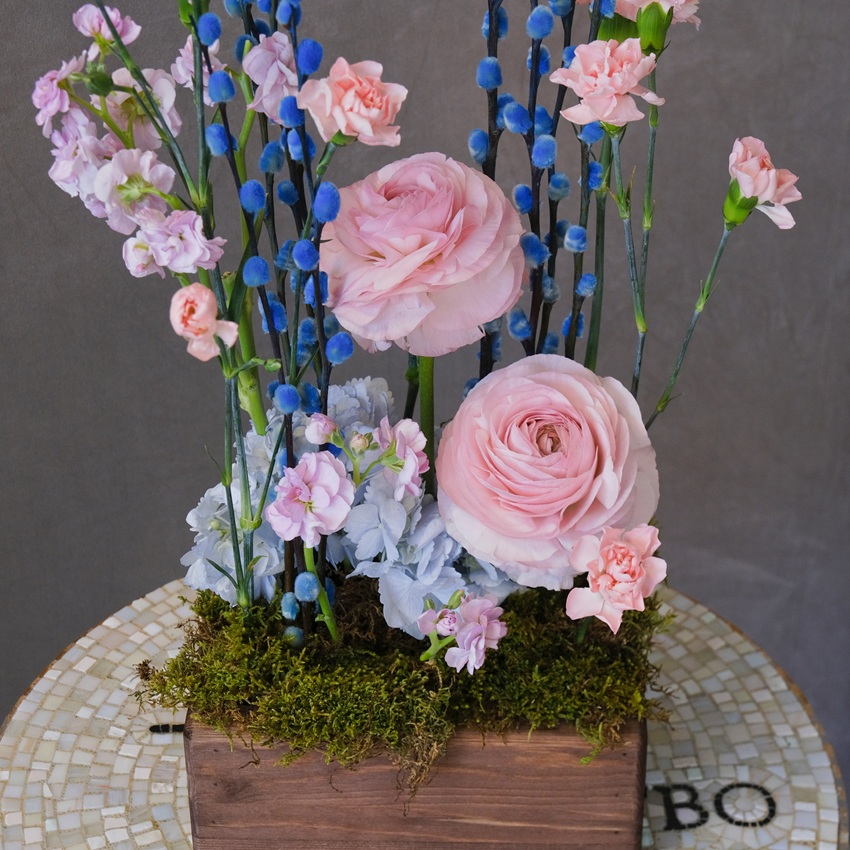  Композиция на Пасху в деревянном ящичке: голубая верба, ранункулюсы и гвоздики 