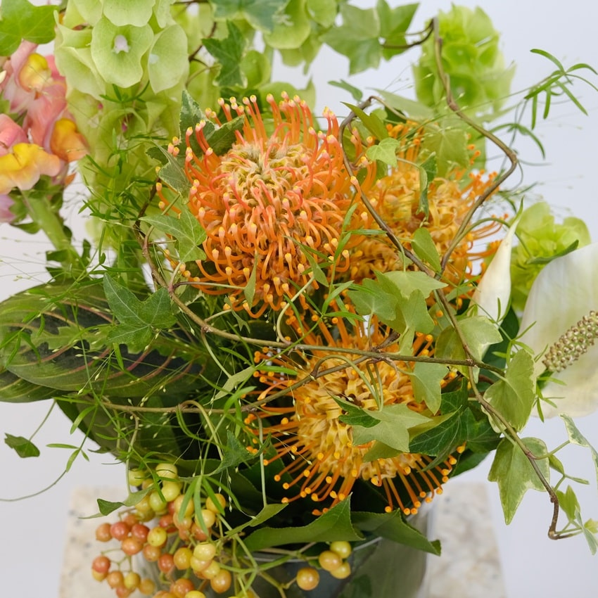 Экзотическая композиция для интерьера в стеклянной вазе: моллюцелла, нутан и антирринум